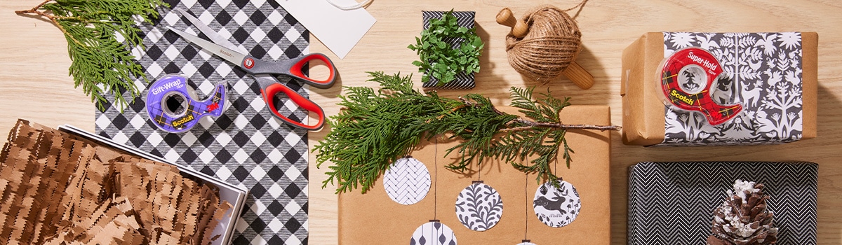 Mesa con envolturas de regalo y cintas adhesivas Scotch morada y roja.
