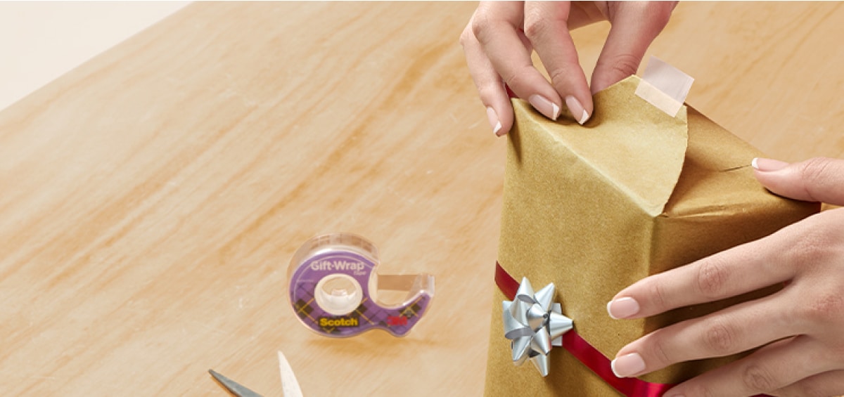 Manos sosteniendo un regalo con cinta morada en la mesa.
