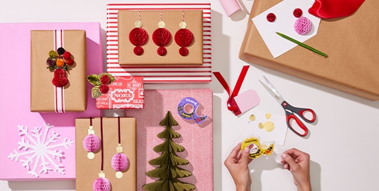 Manos sosteniendo cinta amarilla con regalos navideños a un lado.
