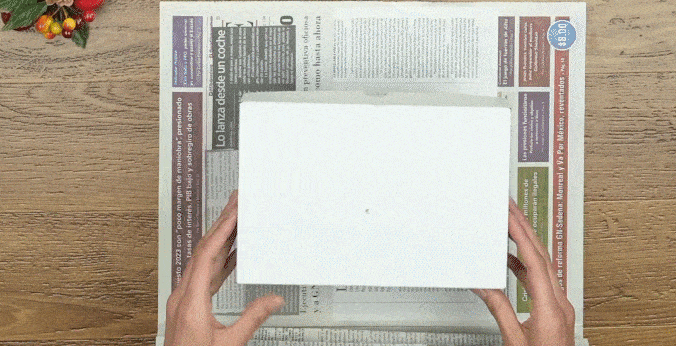 Manos de mujer envolviendo una caja con papel periódico con Cinta Súper Adhesiva Scotch®.
