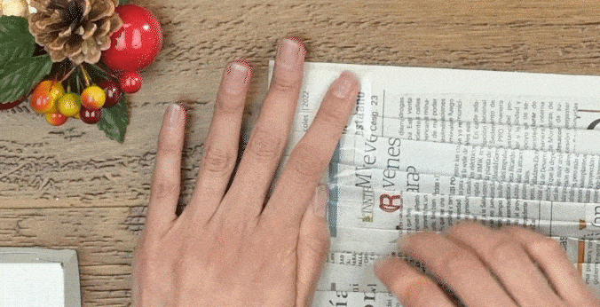 Manos de mujer doblando una hoja de papel periódico.
